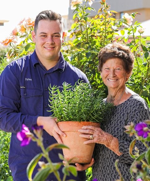 A gardener and a resident holding a potted herb together