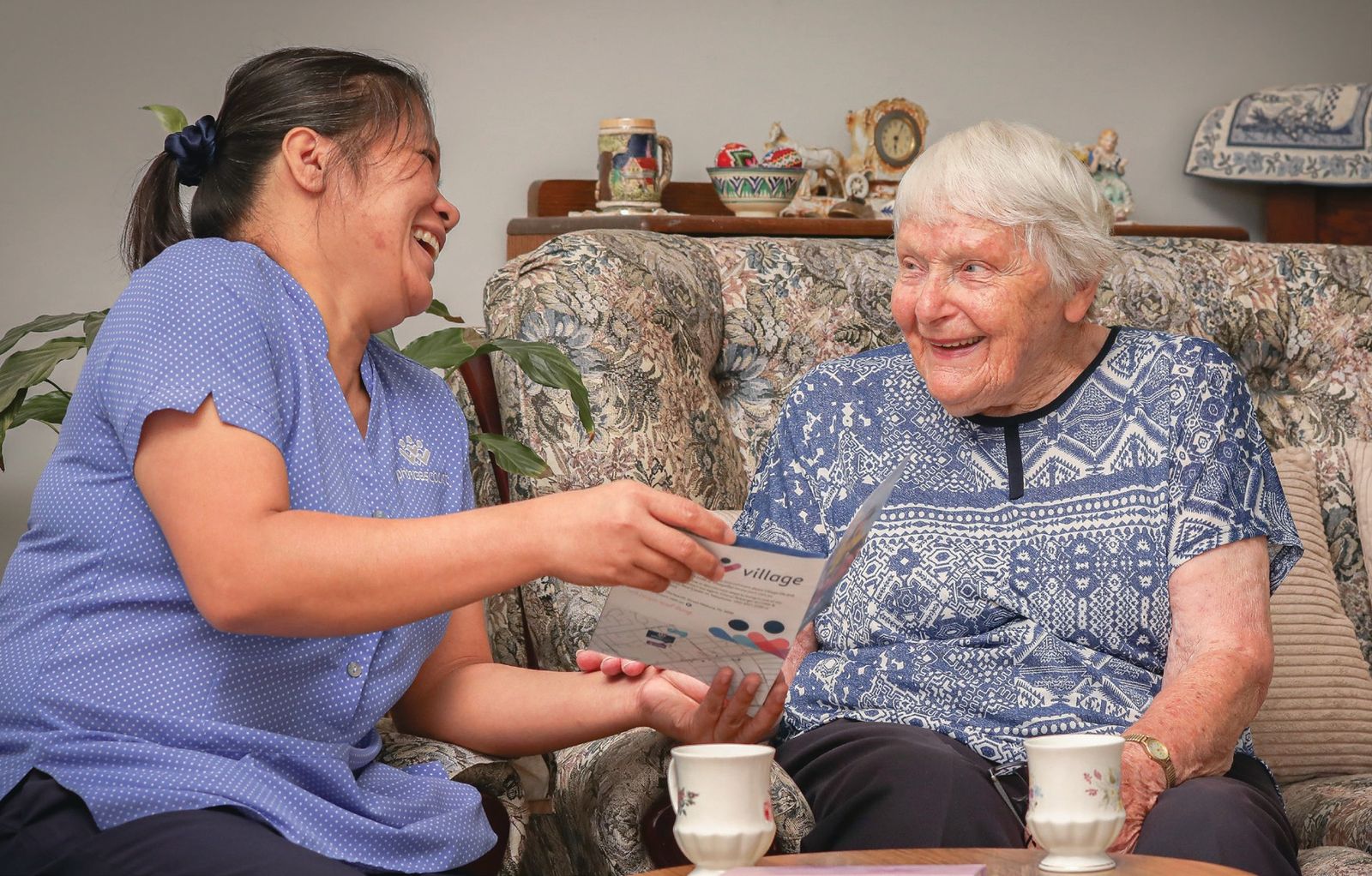 A carer laughing with a client over a card at her kitchen table