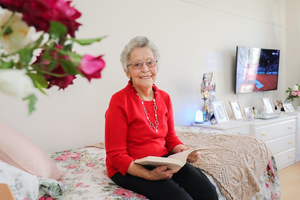 A resident reading a book on her bed in her bright private room