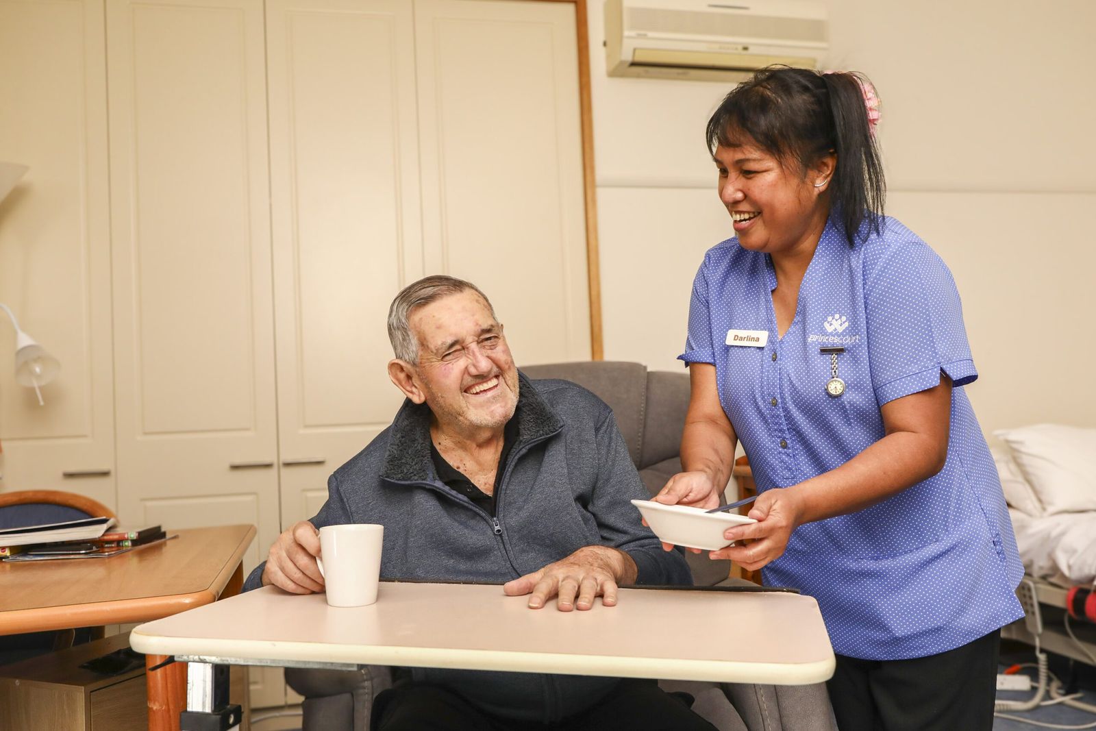 A carer bringing a smiling resident his morning tea